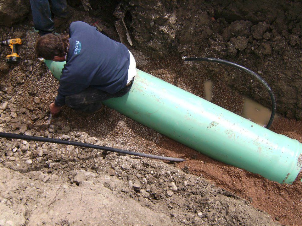 Worker inspecting a large green pipe in a muddy trench during excavation work