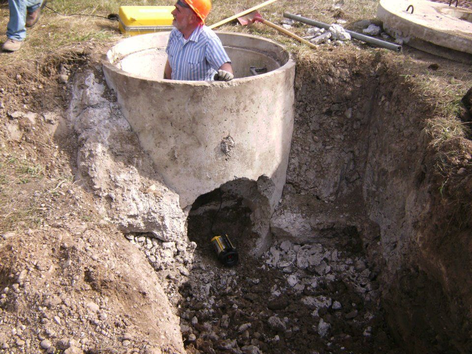 Worker in orange hard hat inside concrete manhole during excavation at a construction site