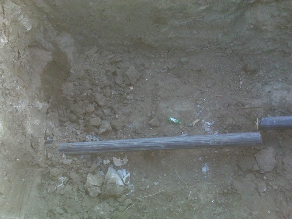 A metal pipe lying across a dirt trench with rocky soil around it.