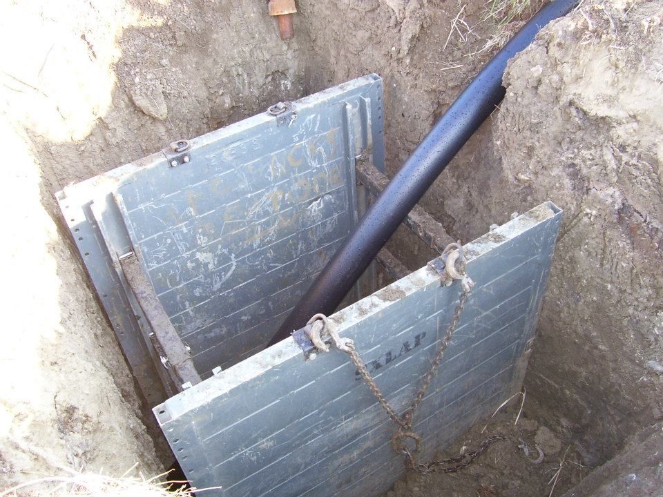 Damaged metal utility box in a dirt excavation with a black pipe running through it