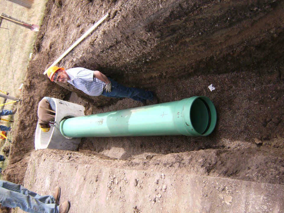 Worker beside a large green pipe laid in a dirt trench at a construction site