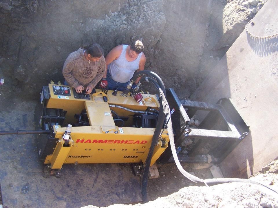 Workers operating a yellow construction machine inside a deep trench
