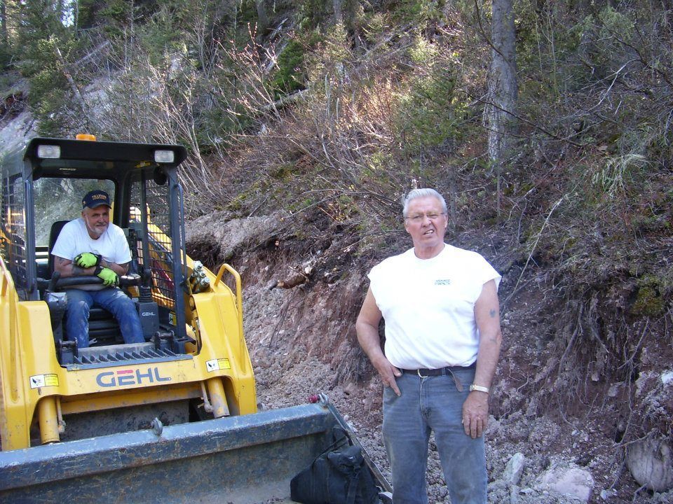 Yellow GEHL bulldozer beside a man standing on a rocky dirt road in a wooded area
