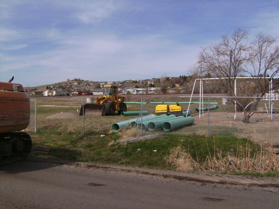 Rural yard with farm equipment, green pipes, yellow tanks, and a white goal frame under a cloudy sky