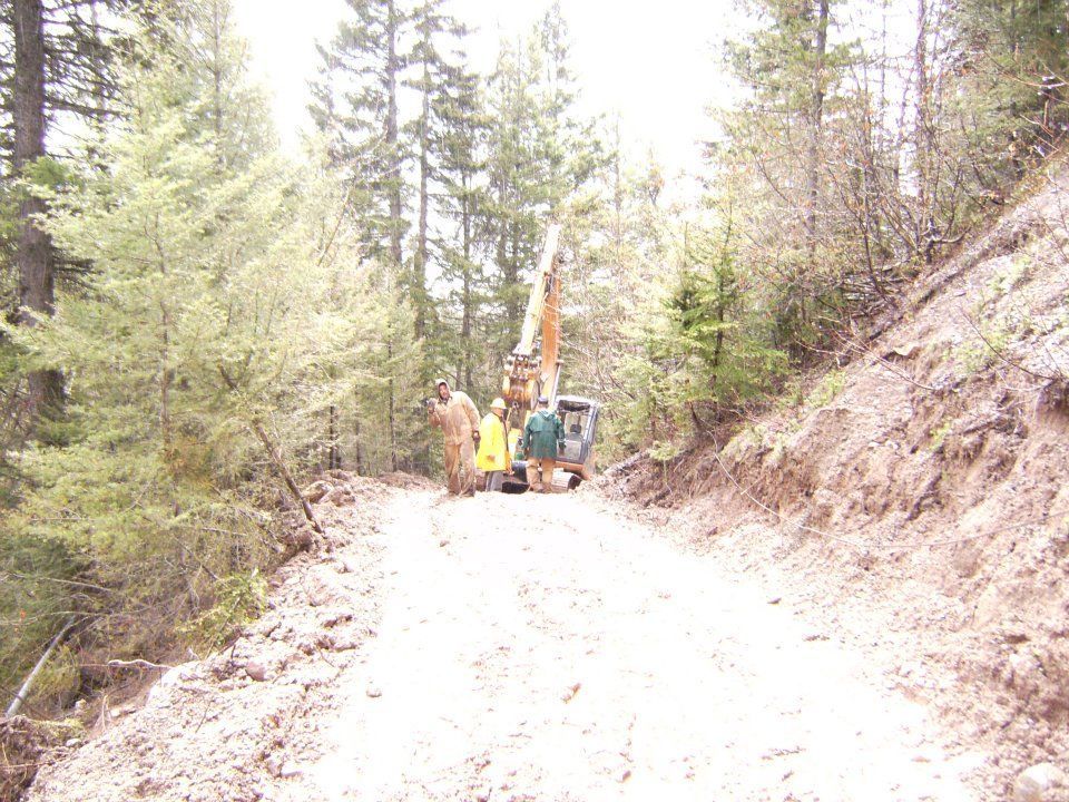 Construction workers and excavator repairing a dirt road in a wooded area