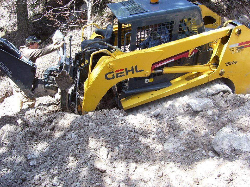 Yellow Gehl skid steer digging through rubble on a rocky debris pile