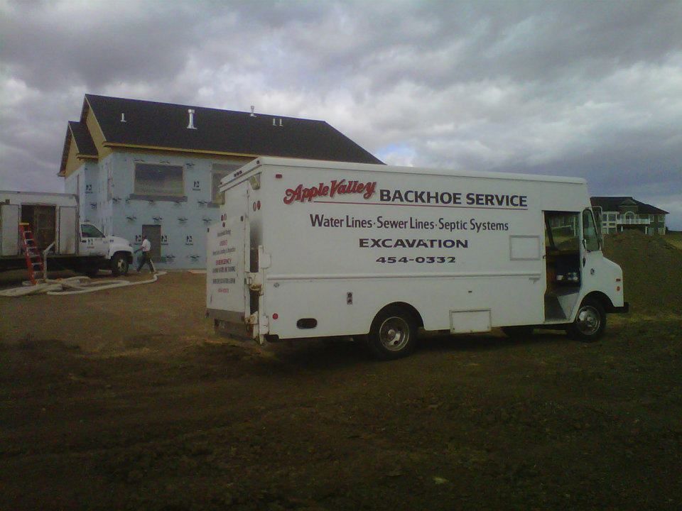 White service truck parked outside a building, with a sign for “Backhoe Service” on the side.