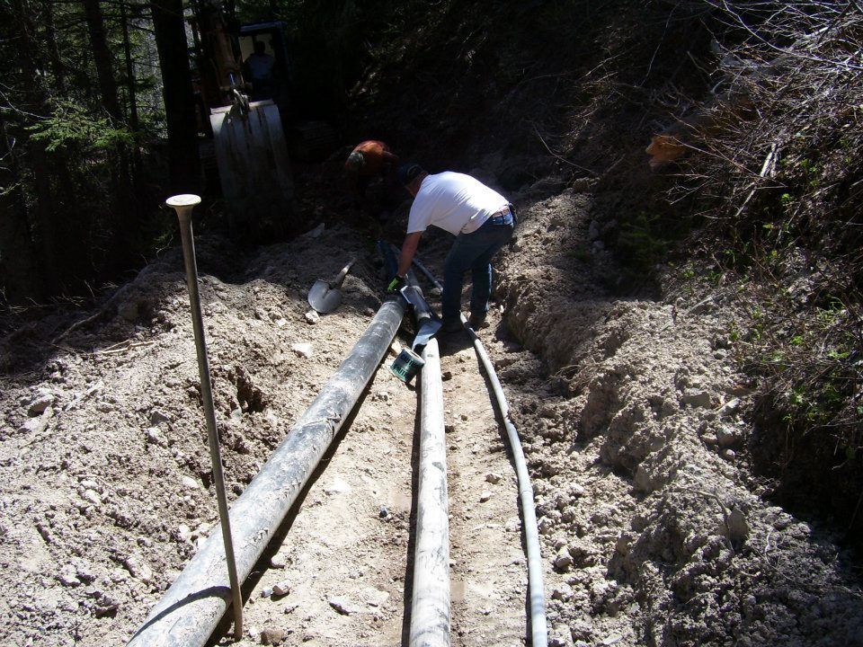 Workers installing large pipes in a dirt trench outdoors