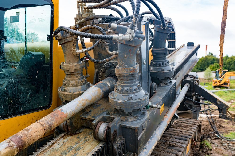 Heavy drilling equipment on a muddy tracked machine beside a yellow vehicle, with hoses and pipes attached