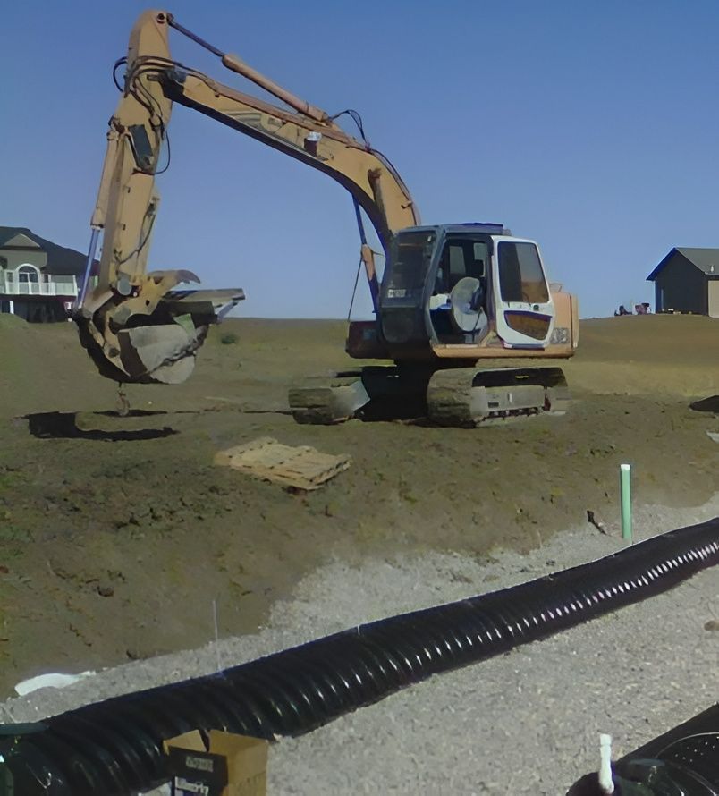 Yellow excavator digging at a construction site with a trench and drainage pipe in the foreground.