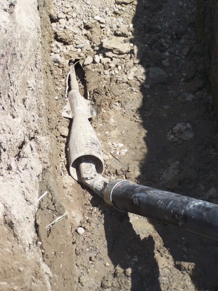 Underground trench with a black pipe inserted into a damaged sleeve or coupling in dirt soil