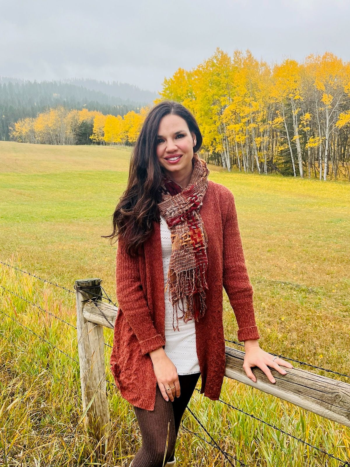 A woman is standing next to a wooden fence in a field.