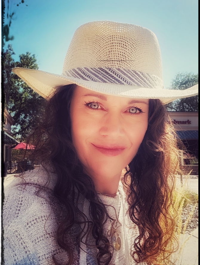 Woman in straw hat smiles, outdoors on a sunny day.