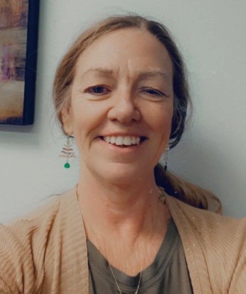 A woman wearing a tan sweater and earrings is smiling for the camera.