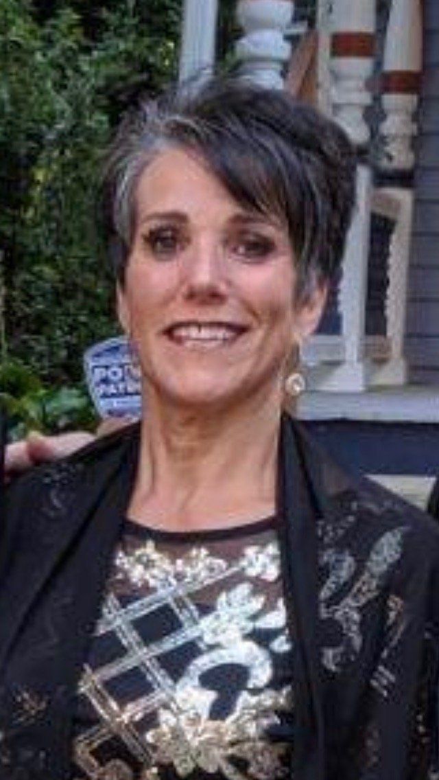 A woman in a black jacket and gold dress is smiling for the camera.
