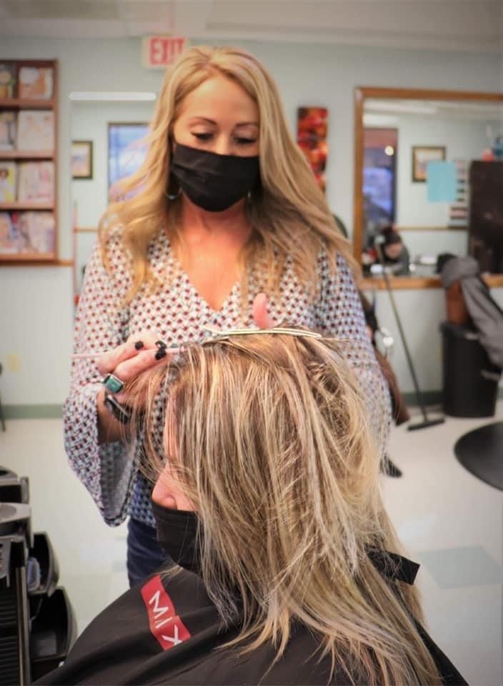 A woman wearing a mask is cutting a woman 's hair in a salon.