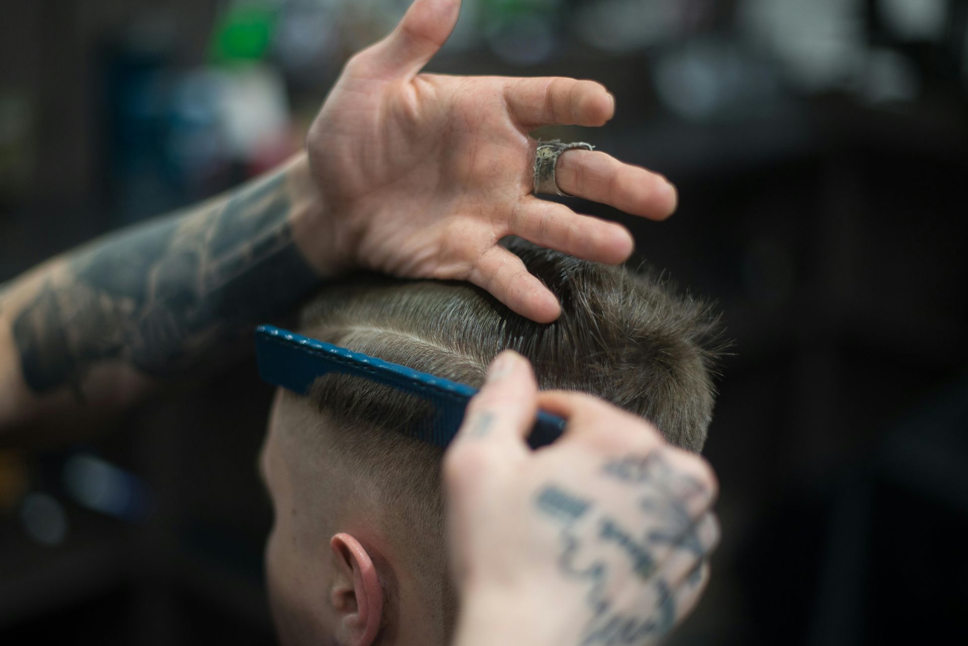 Barber cutting hair with comb and clippers; blurred background of barbershop.