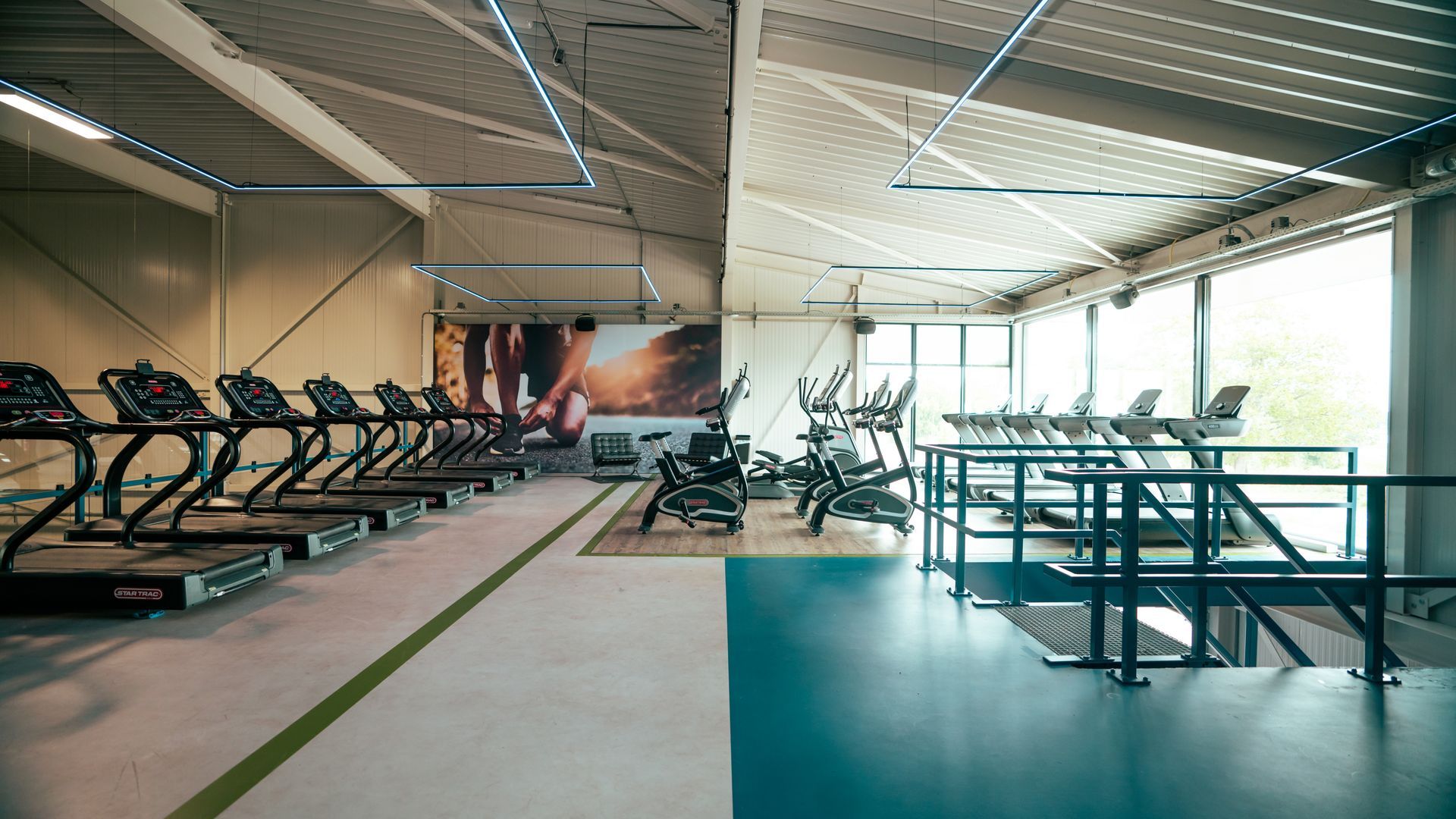 Moderne fitnessruimte met loopbanden, hometrainers en gewichtsapparaten in een lichte, open ruimte.