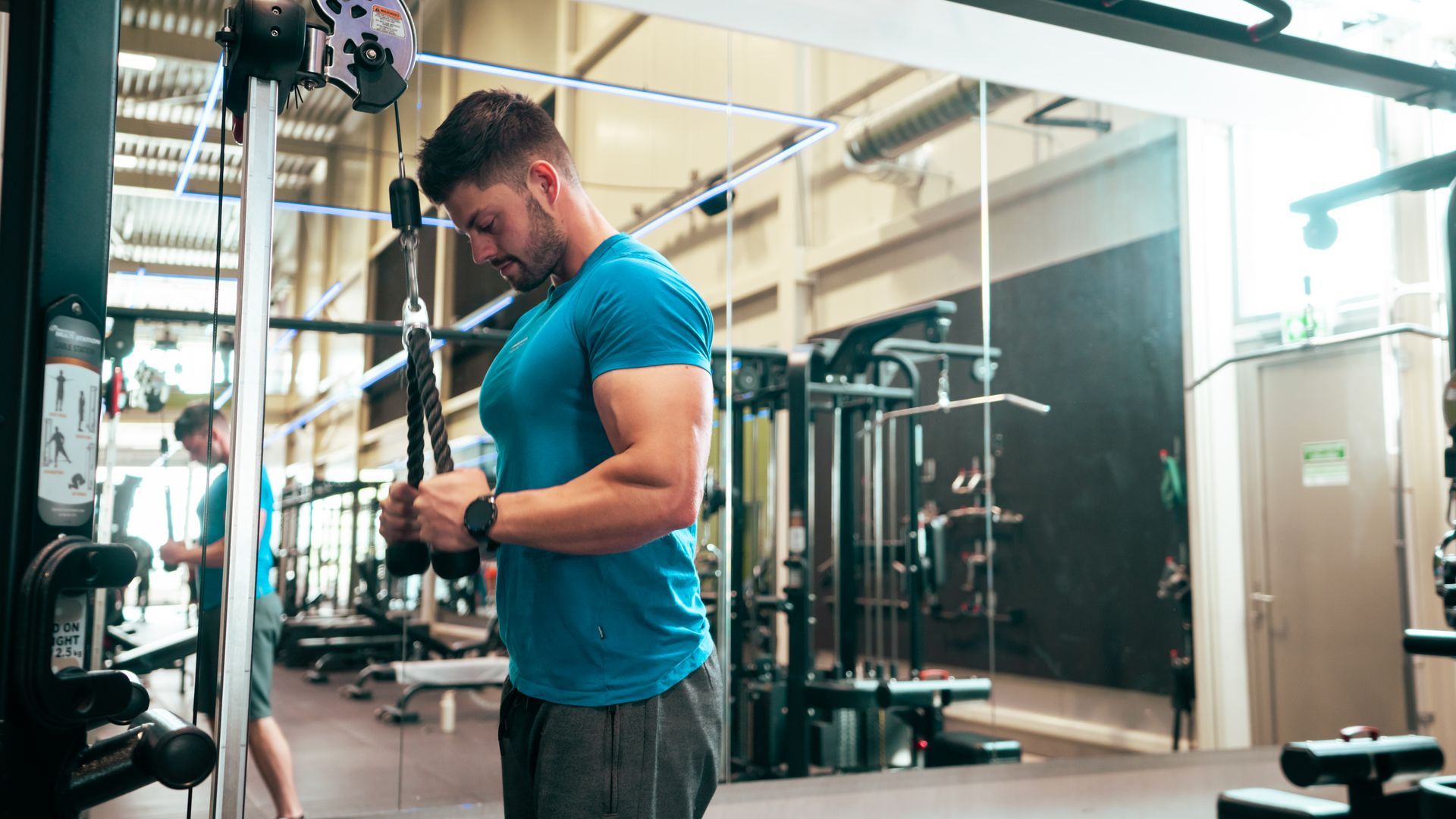 Een man in een blauw shirt gebruikt een kabelmachine in een sportschool en is geconcentreerd op zijn training.