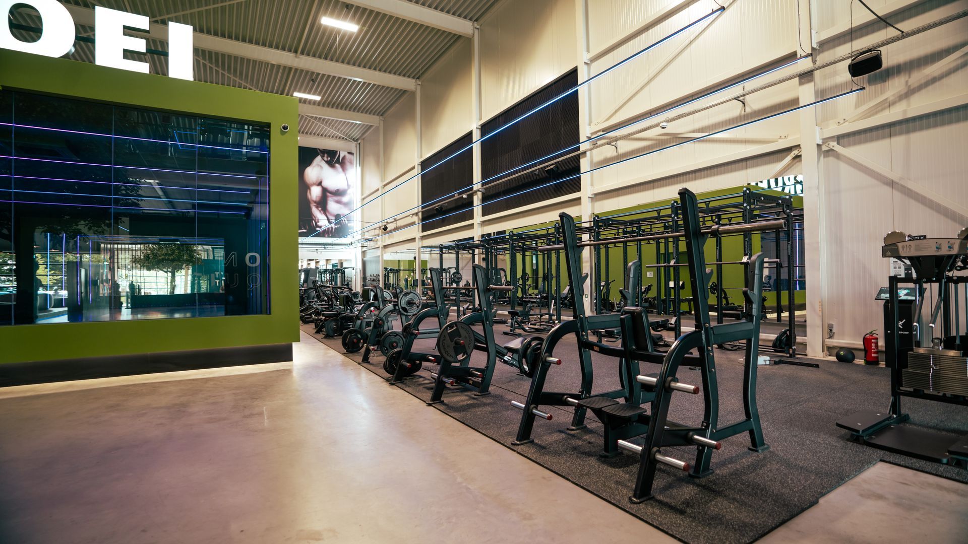 Modern fitnesscentrum met rijen gewichtsapparaten en losse gewichten op een zwarte matvloer.