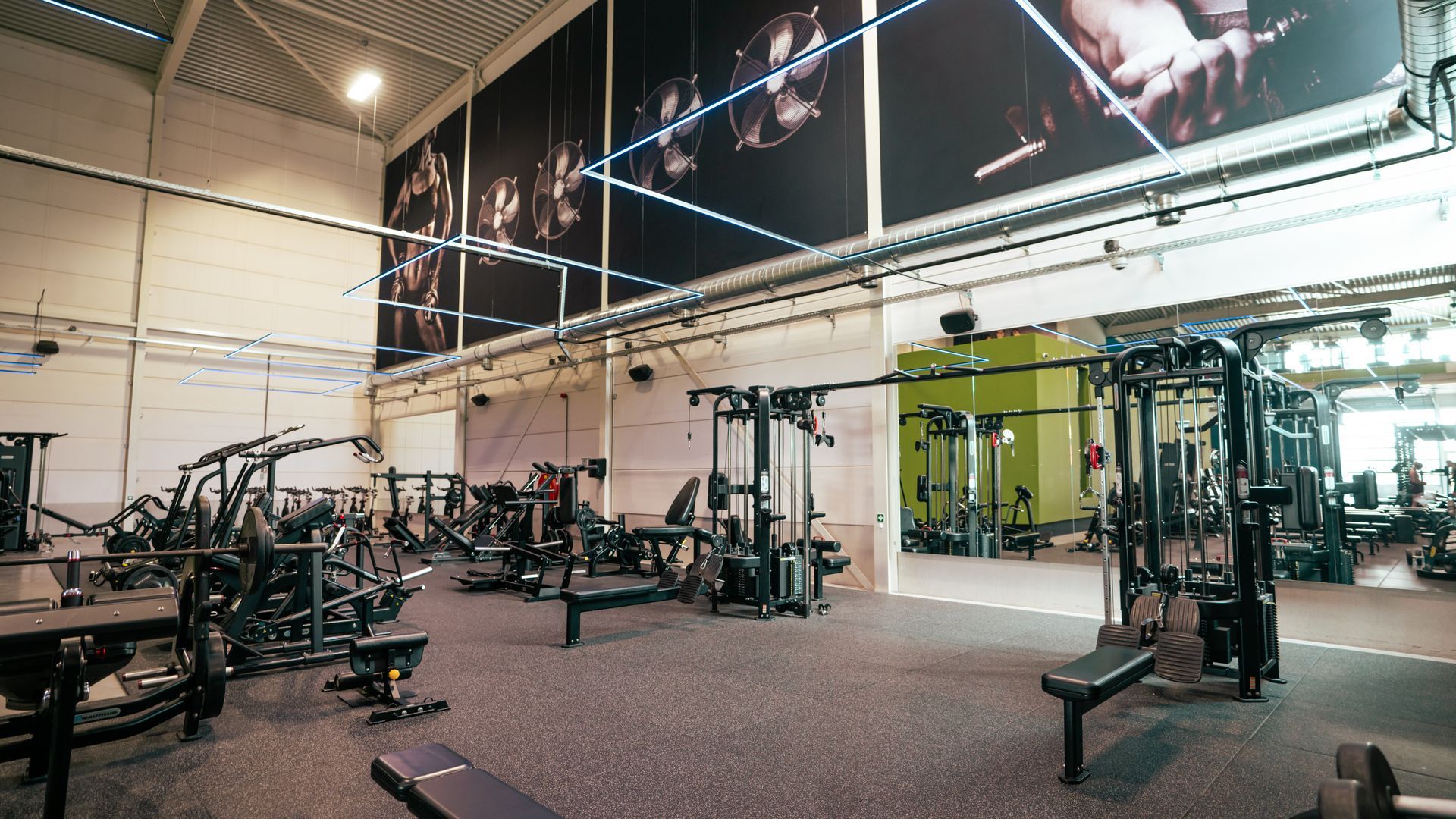 Ruime fitnessruimte met gewichtsapparaten, banken en grote fitnessmuurschilderingen.