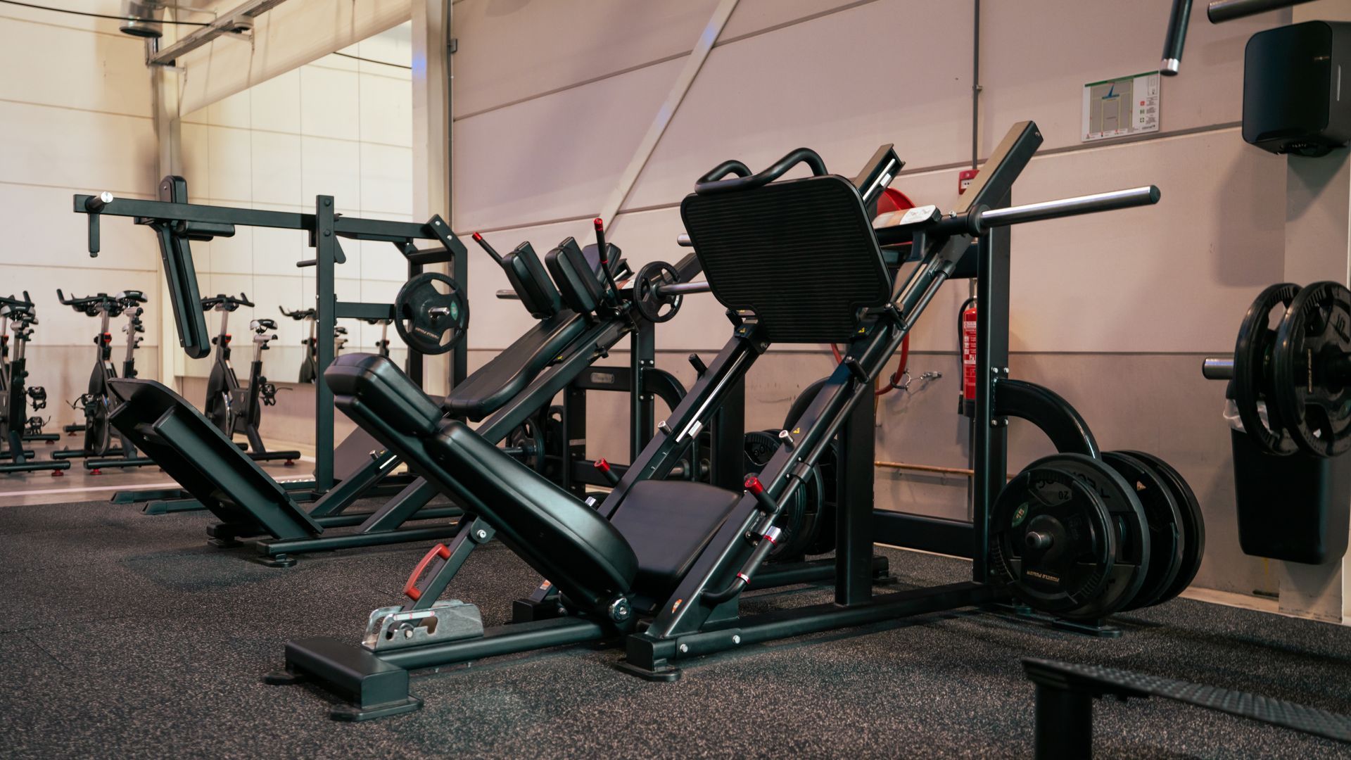 Zwart-rode leg press machine in een sportschool met halters en gewichtsschijven.