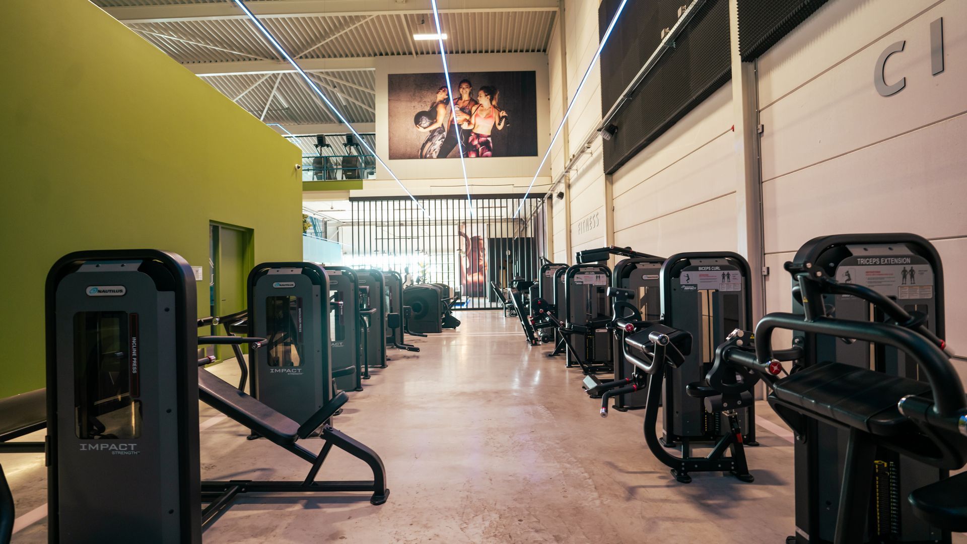 Binnengym met rijen fitnessapparaten op een gepolijste vloer en een hoog plafond.