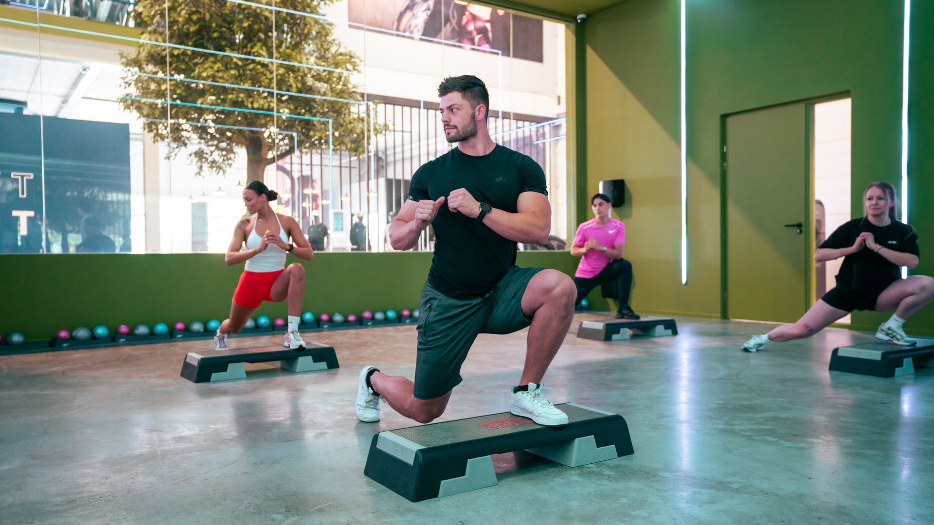 Mensen doen step-aerobics in een lichte fitnessstudio met grote ramen.