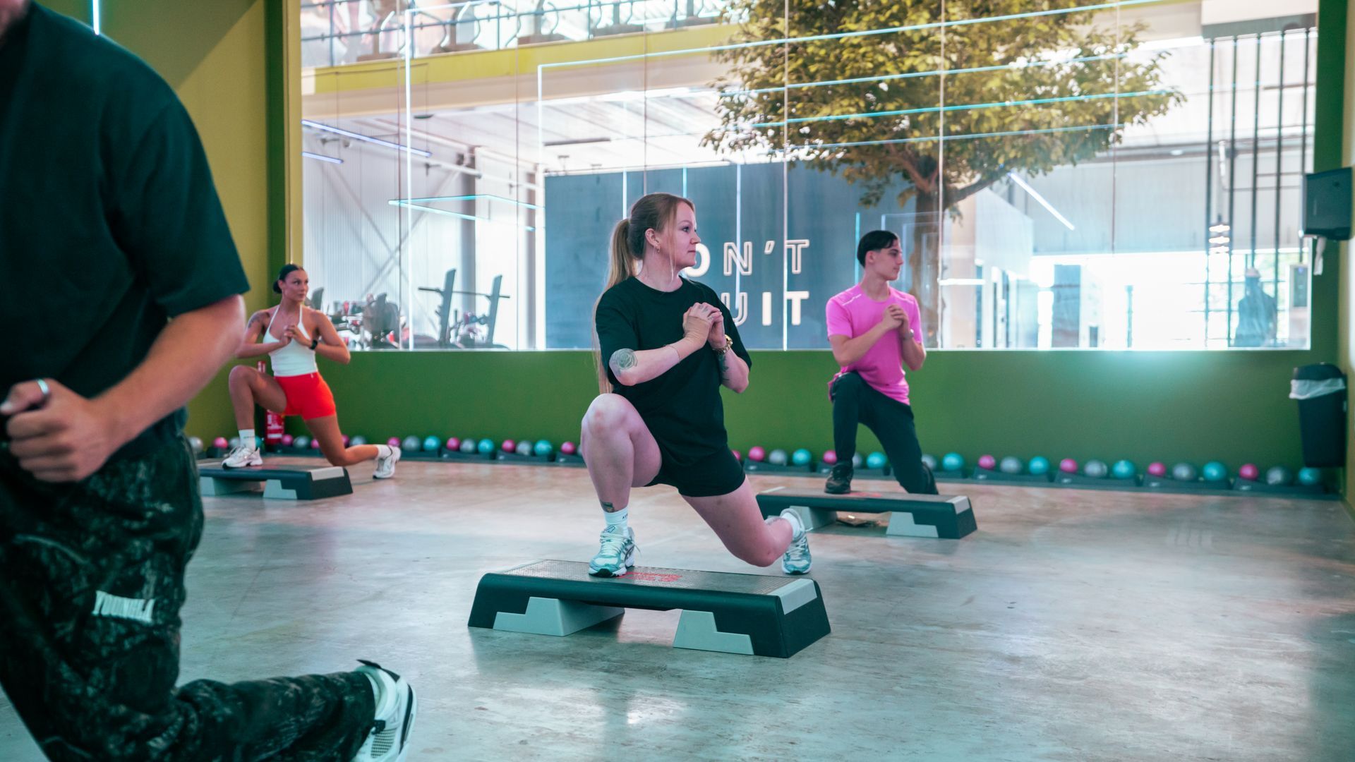 Mensen doen step-aerobics in een lichte sportschool met grote ramen.