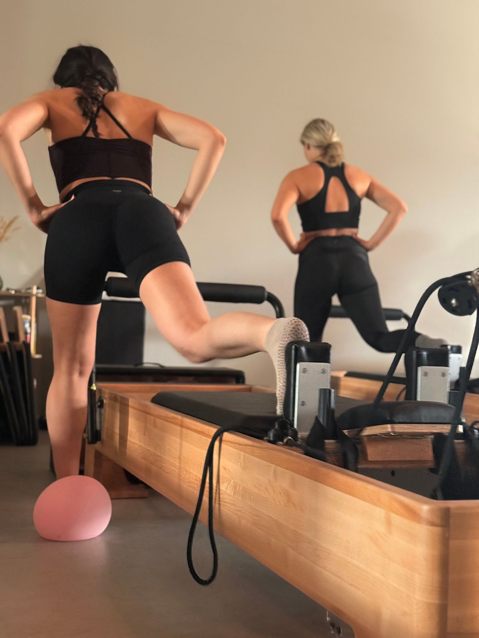 Twee vrouwen in zwarte sportkleding doen oefeningen op Pilates-apparaten in een studio.