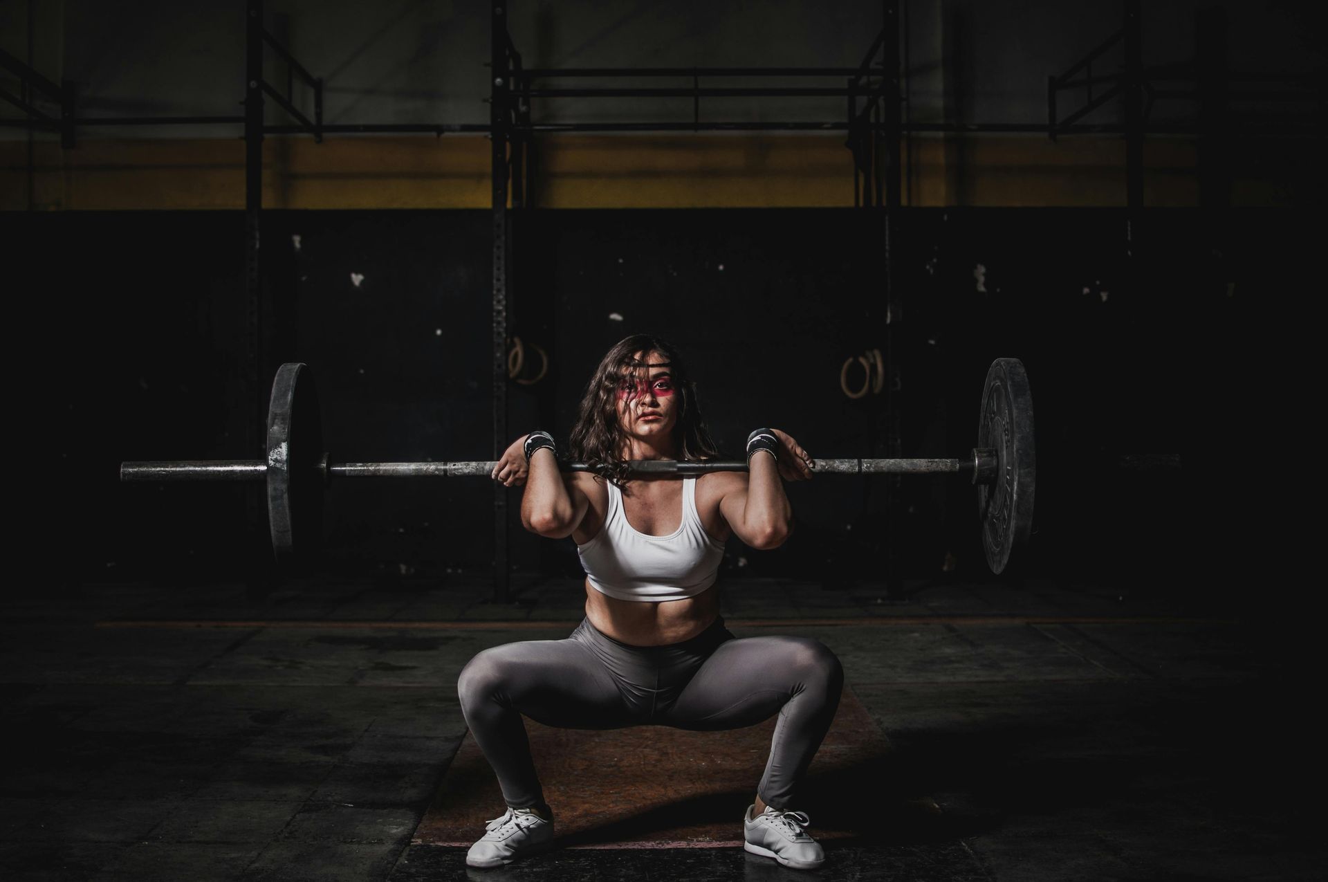 Een vrouw doet een squat met een halter boven haar hoofd in een sportschool.
