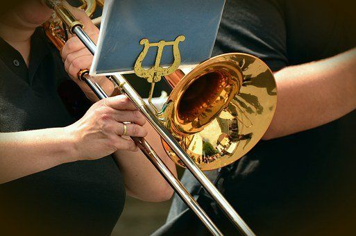 Een persoon die op een koperen trombone speelt, met een close-up van de beker en de schuif.
