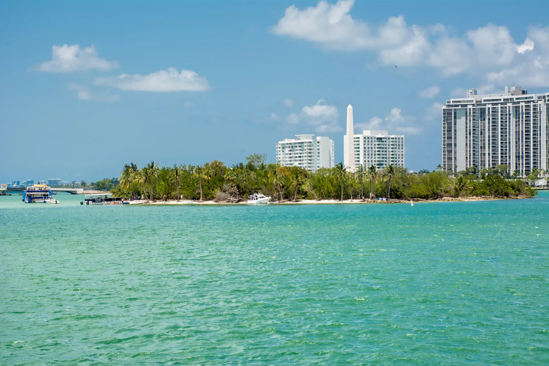 The Henry Flagler Monument on Monument Island surrounded by turquoise waters in Miami with the city skyline in the background.