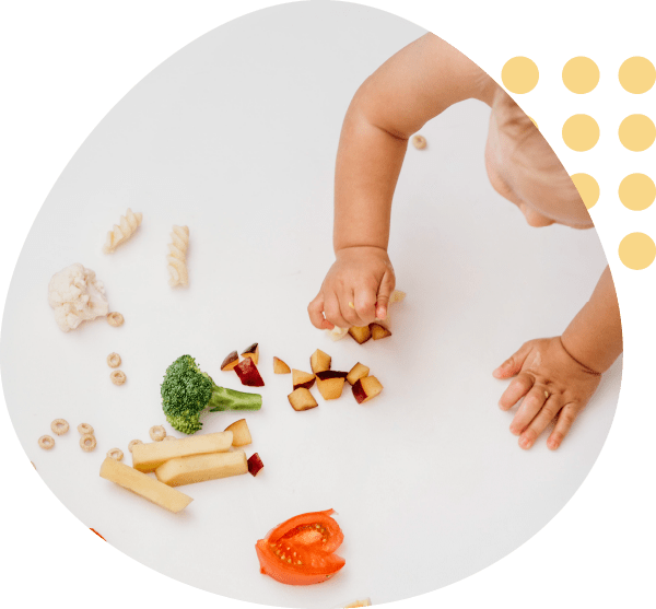 A baby is playing with vegetables on a white surface.
