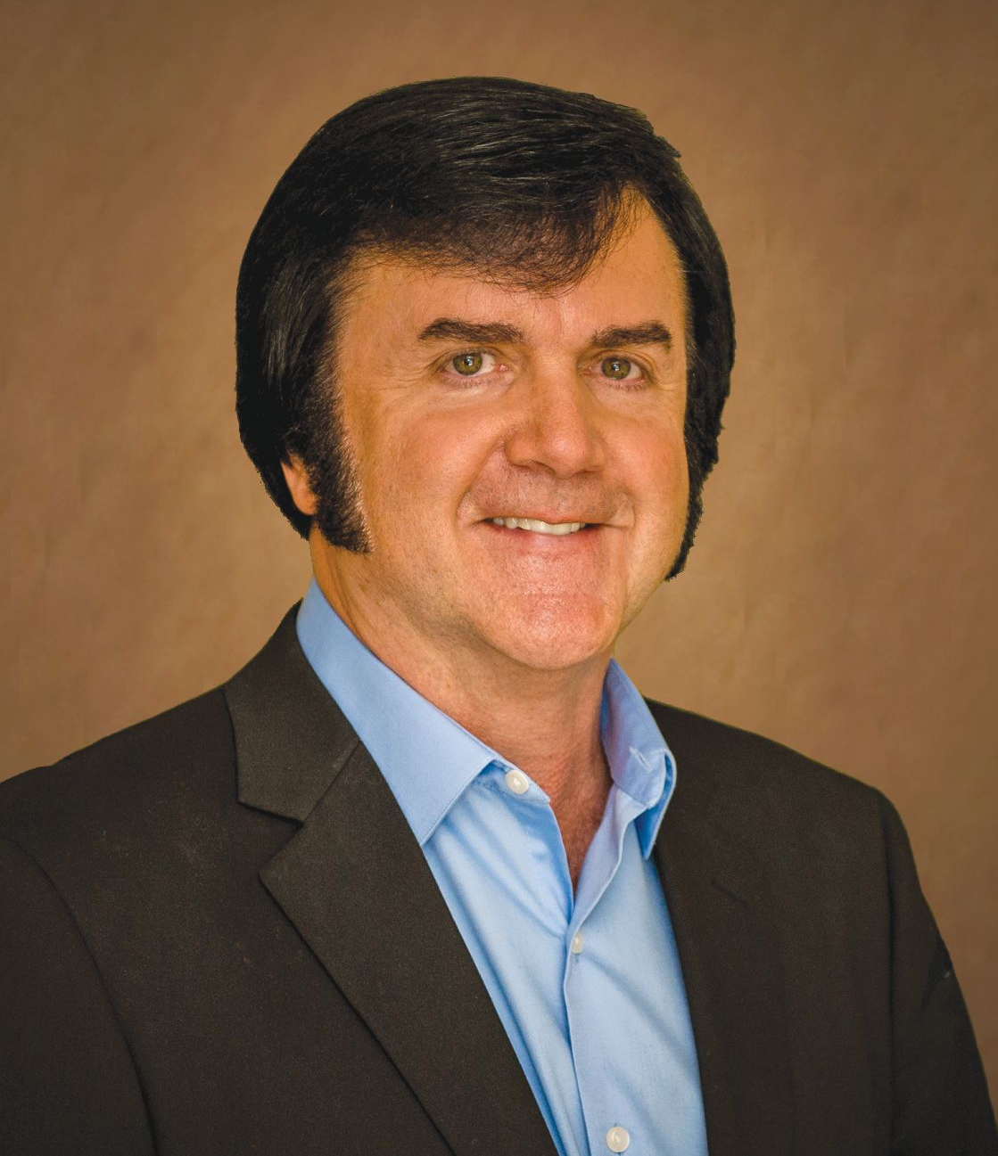 Studio portrait of a man in a dark suit and light blue shirt against a tan background