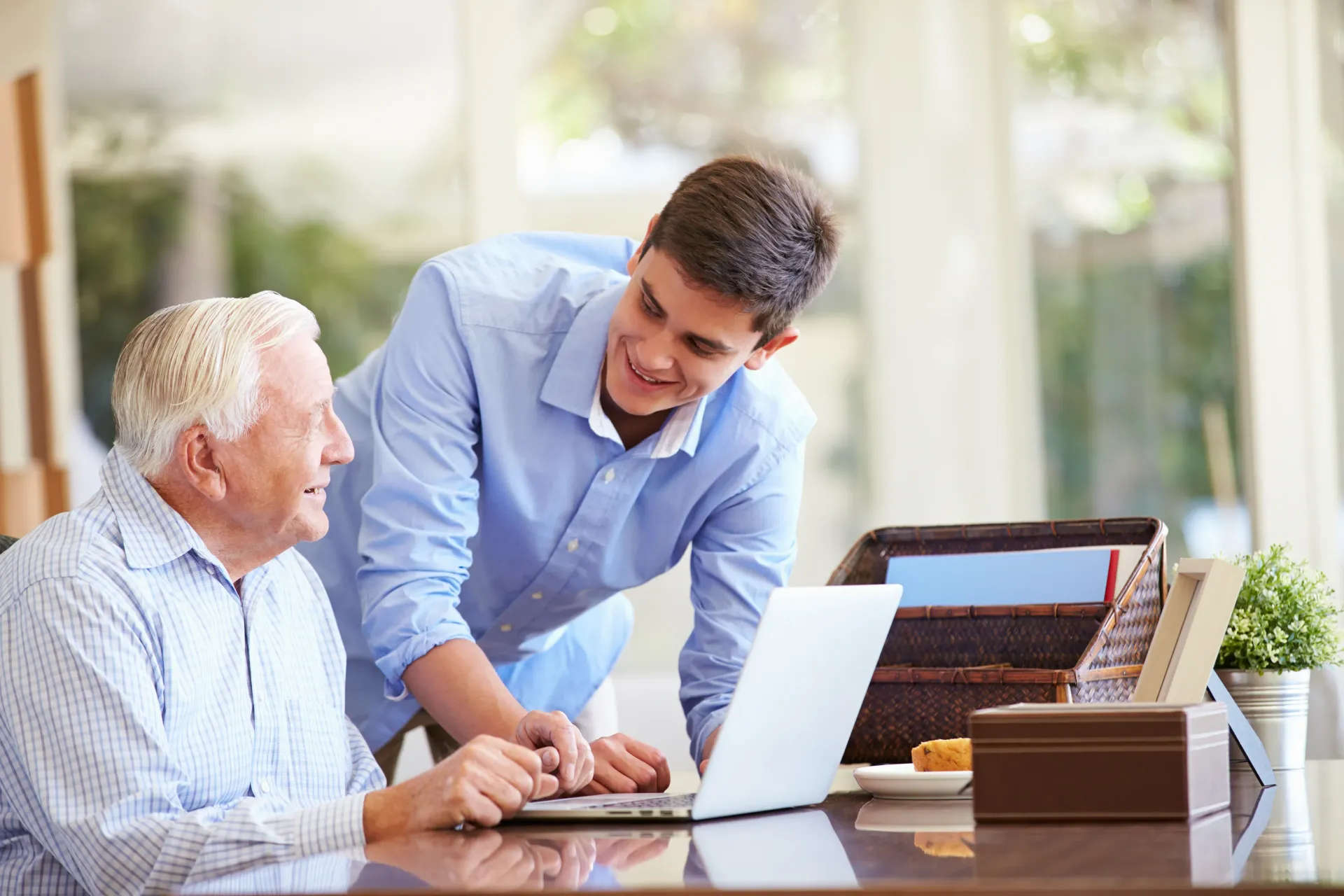 a young man is helping an older man use a laptop computer .