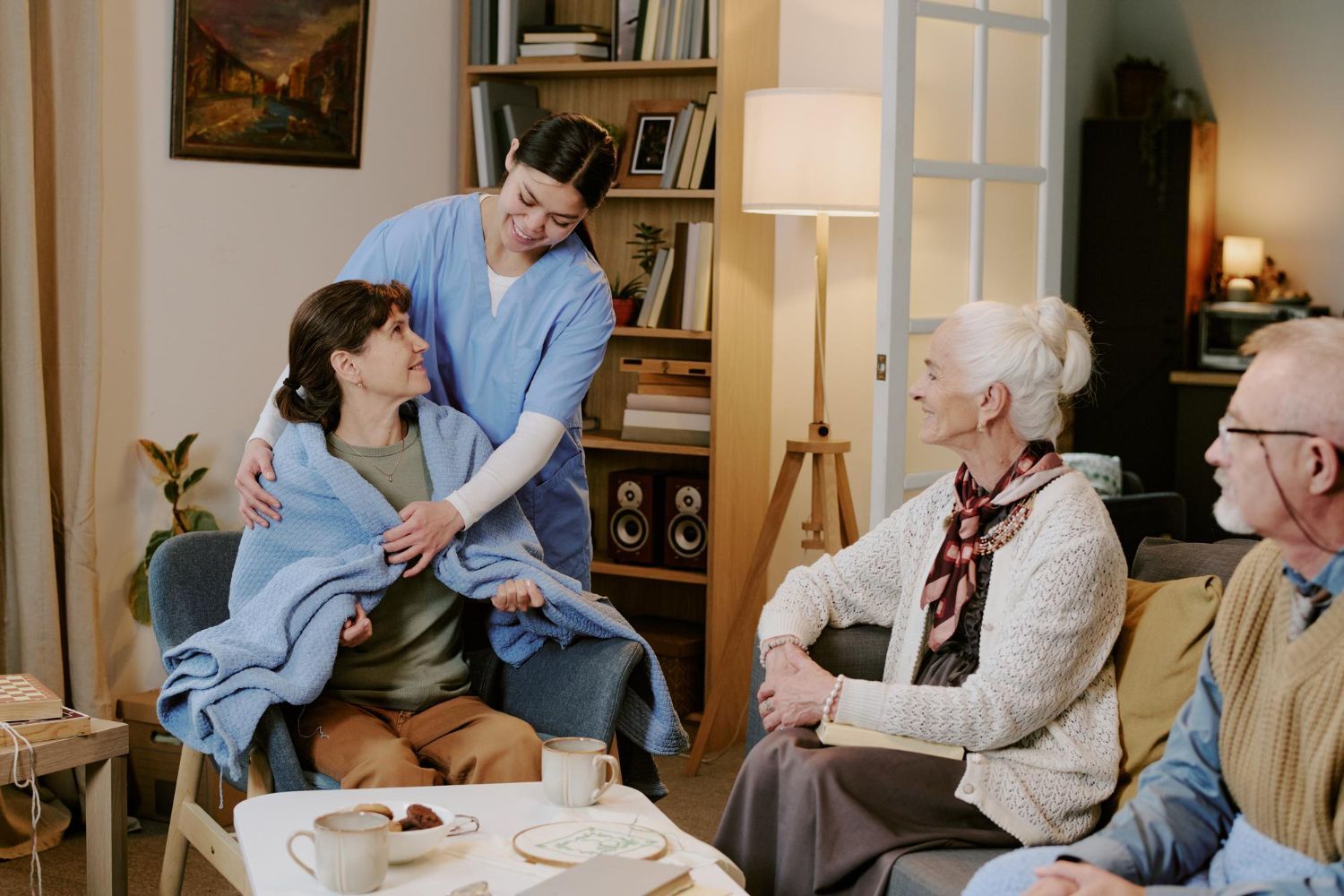Two people sharing a warm embrace in a cozy living room while others sit nearby and watch.