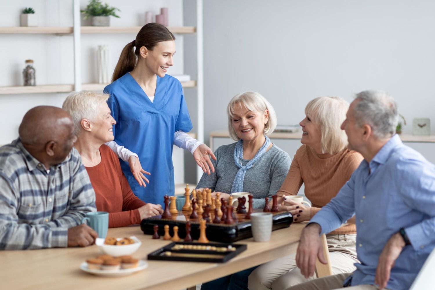 Group gathered around a table with pastries, chatting with a woman in blue in a bright living room