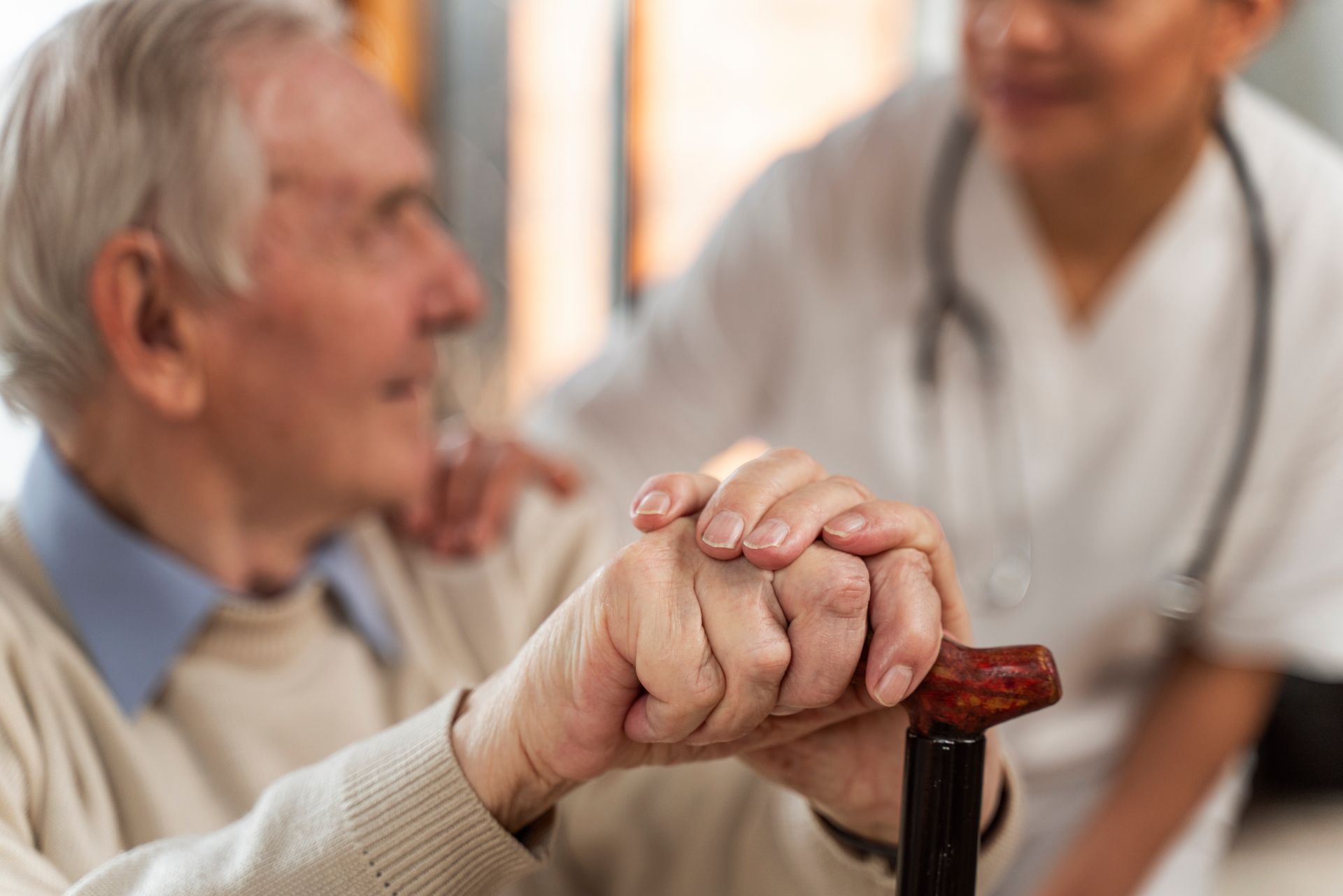A nurse is holding the hand of an elderly man holding a cane.