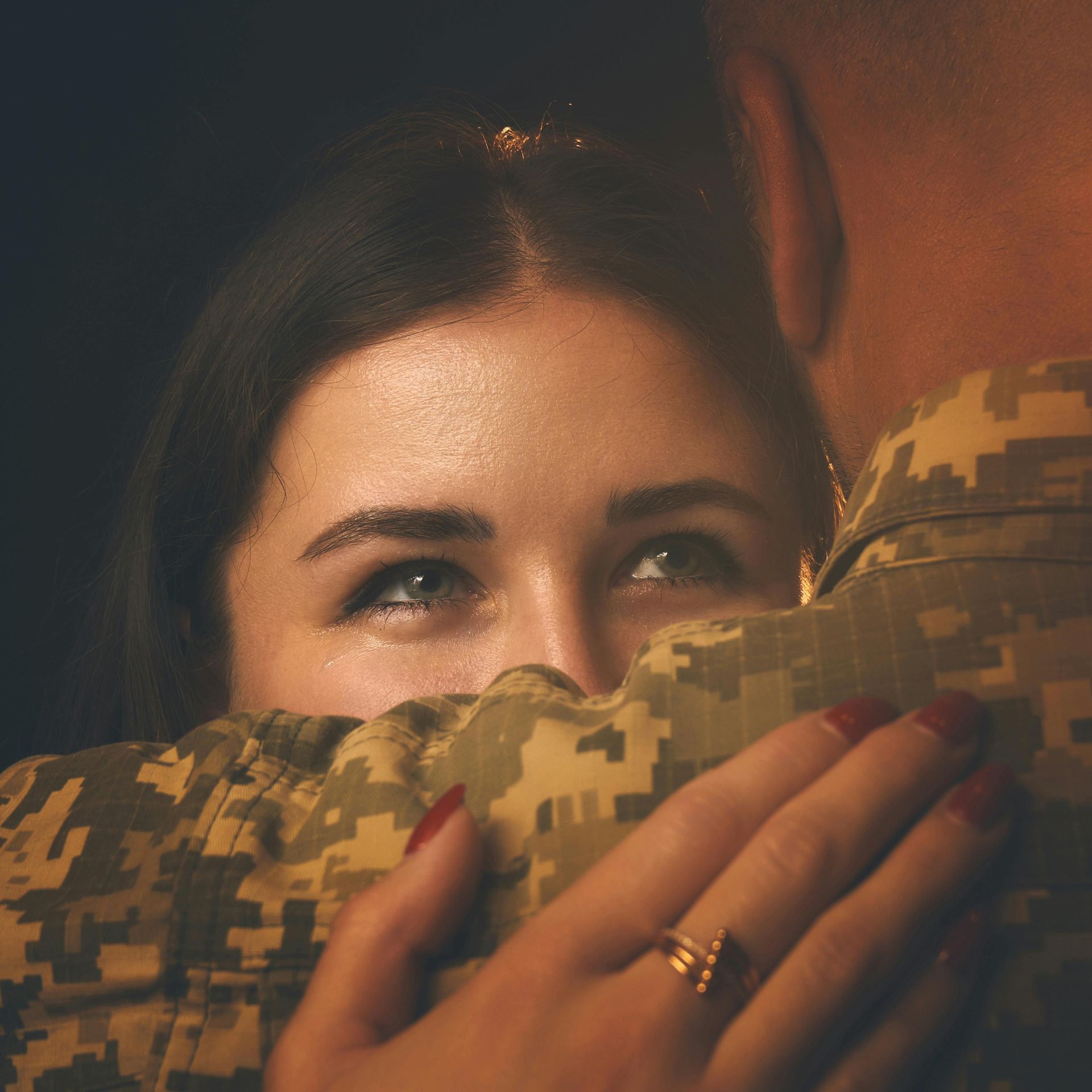 MilSpouse hugs a soldier, eyes teary, in a warm close-up hug