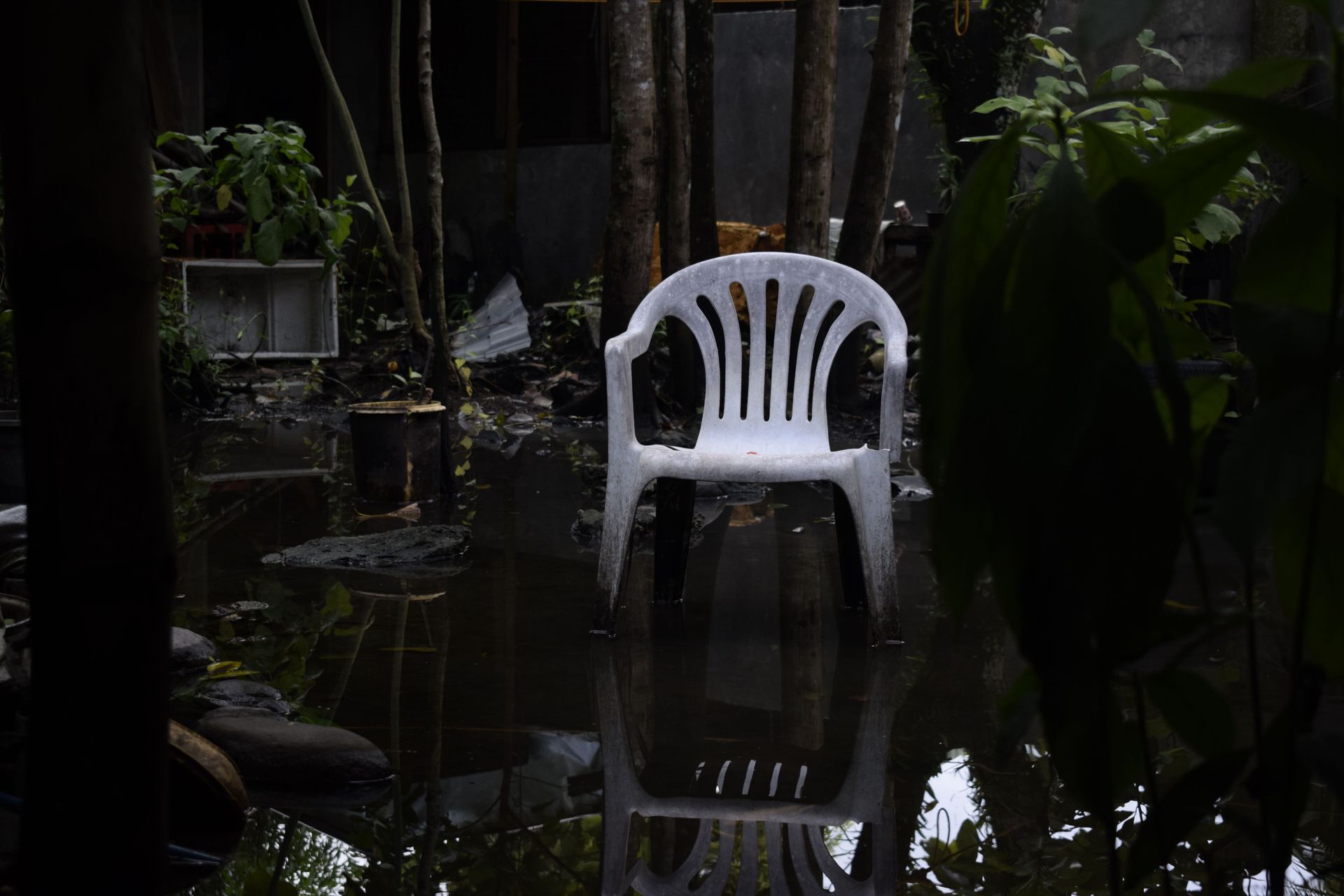 White plastic chair standing in a dark flooded garden with dense greenery around it