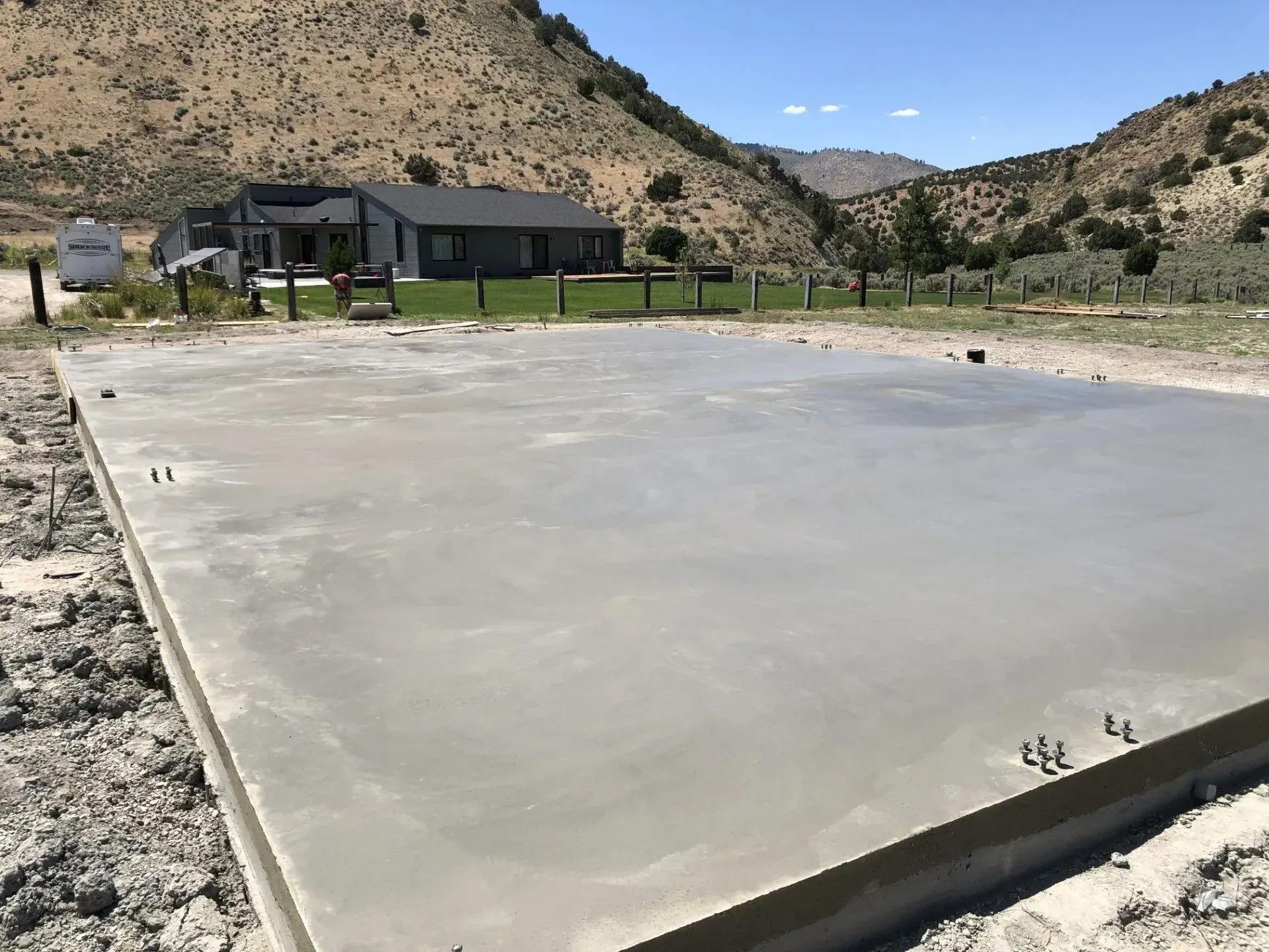 New concrete slab in a rural desert lot with hills and a small building in the background
