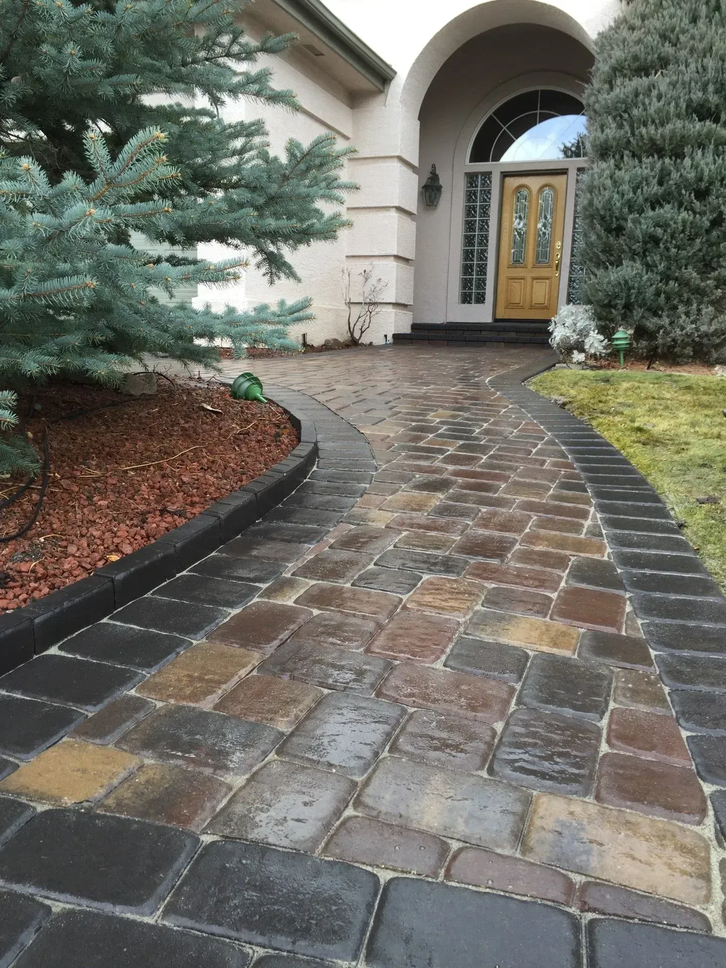 Brick walkway leading to an arched front door, lined with evergreen shrubs and red mulch