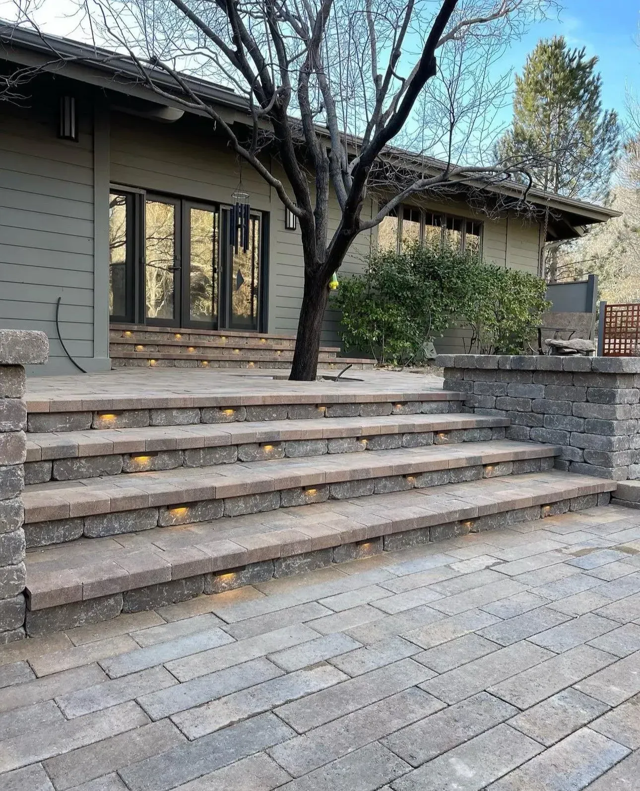 Stone steps leading to a house patio with a tree, shrubs, and large glass doors