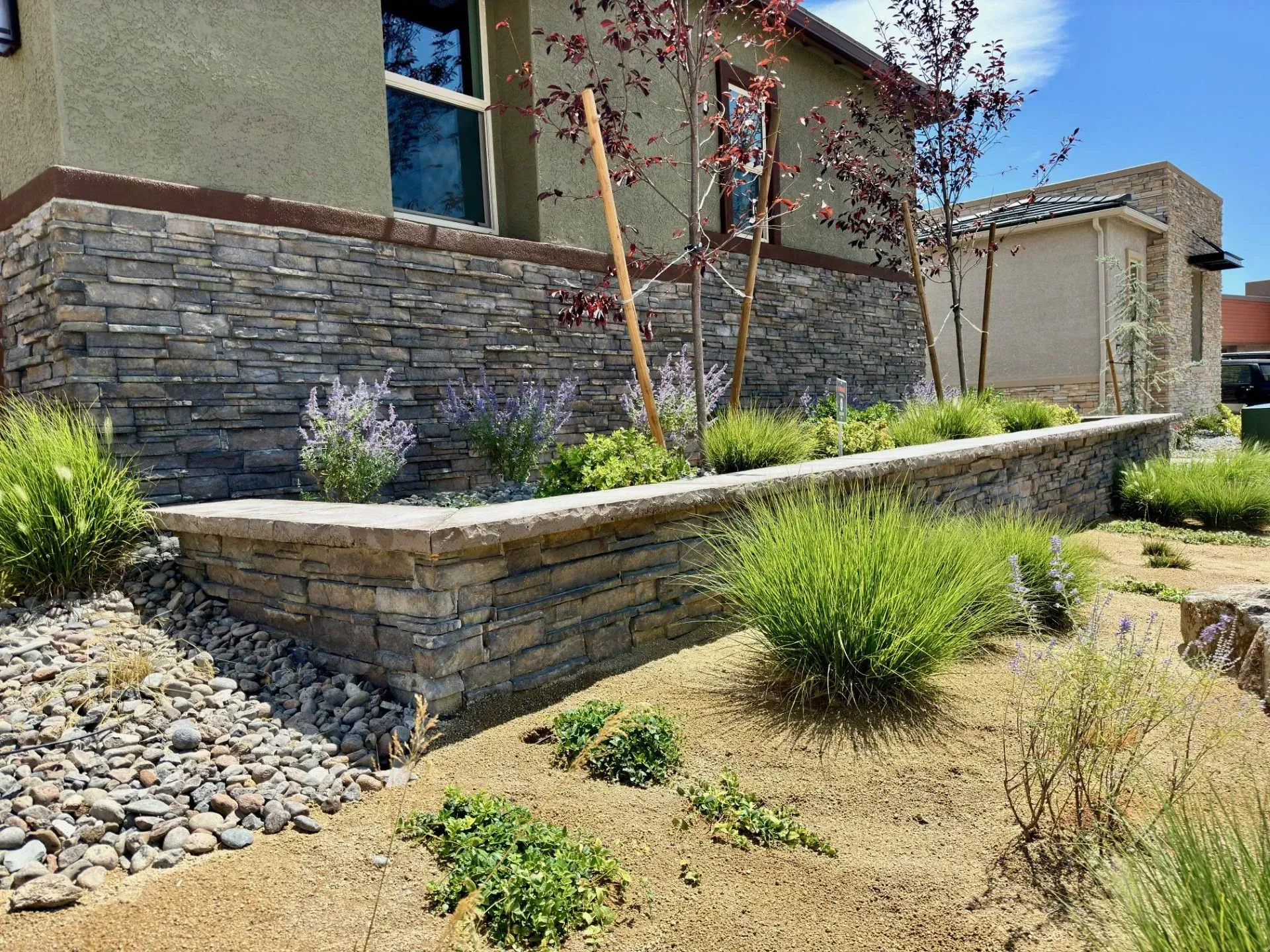 Stone retaining wall and drought-tolerant landscaping beside a stucco house with gravel and shrubs