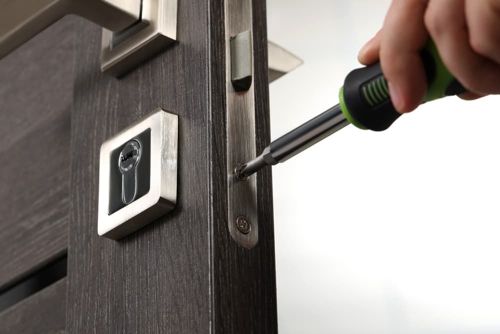 A Person is Fixing a Door With a Screwdriver — Coast & Hinterland Mobile Locksmiths In Cooroy, QLD