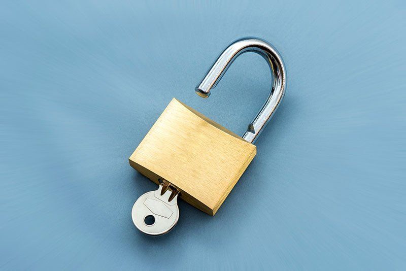 A brass padlock with a key inserted, resting on a smooth blue surface.