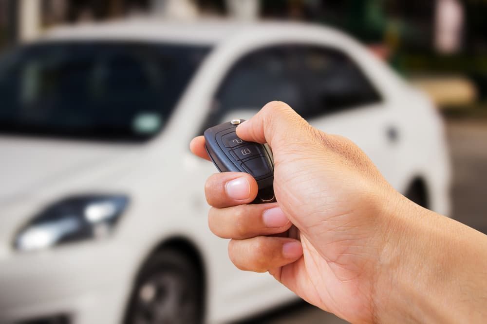 A Person is Holding a Remote Control in Front of a White Car — Coast & Hinterland Mobile Locksmiths In Noosaville, QLD