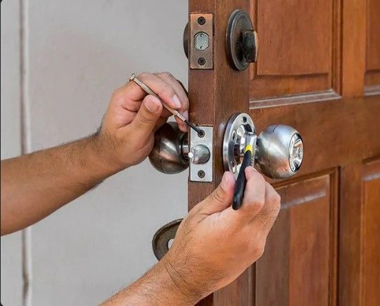 A Man is Fixing a Door Knob With a Screwdriver — Coast & Hinterland Mobile Locksmiths In Coolum, QLD