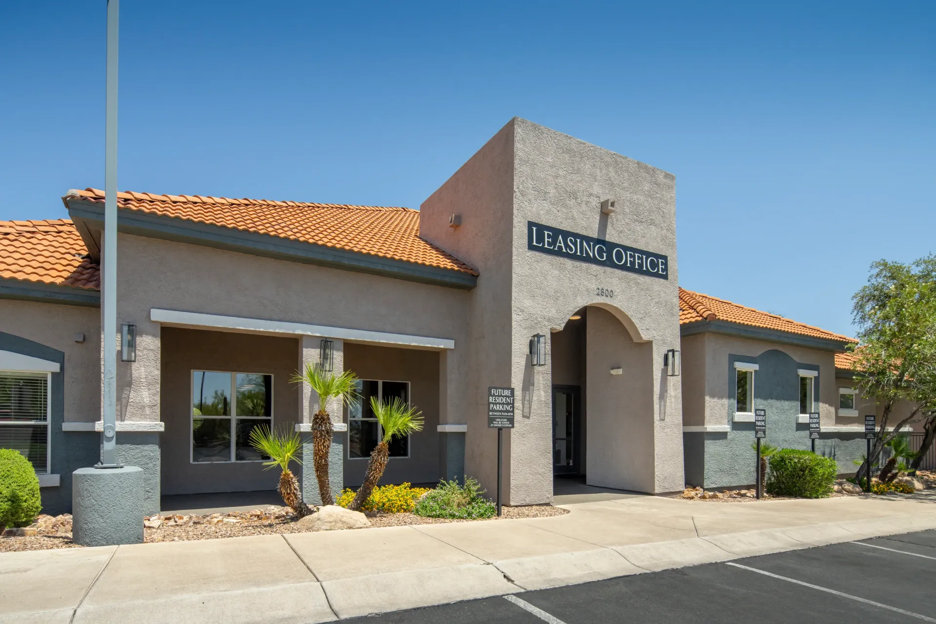 Leasing office building exterior with Spanish tile roof and palm trees at Sonoran Reserve in Tucson, AZ.